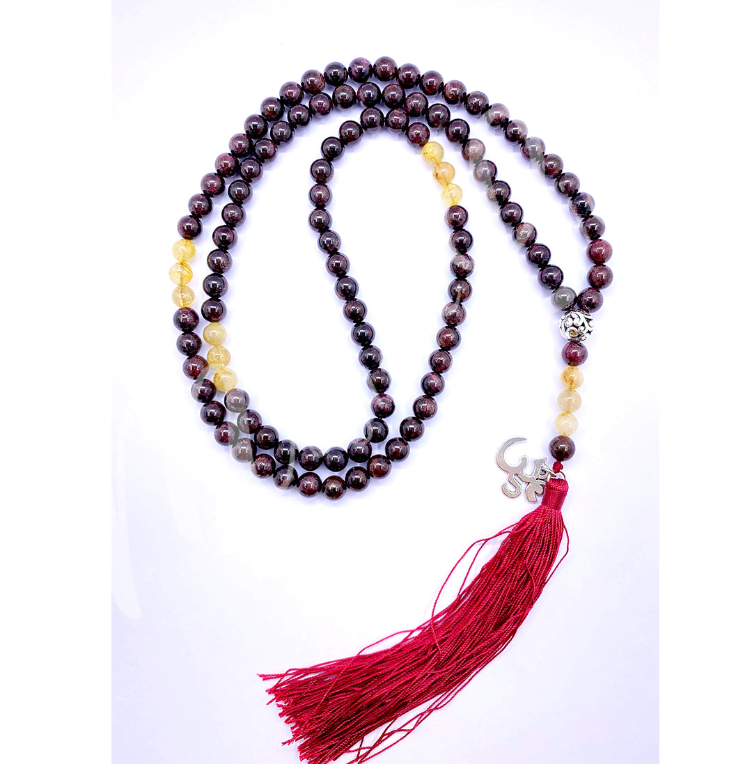 A garnet and rutilated quartz mala necklace with polished round beads with OM charm and a long red tassel.