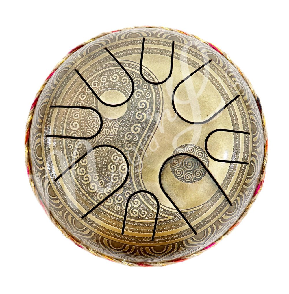A top view of an iron tongue drum with a speckled finish, featuring multiple U-shaped cutout tongues and an ying yang design.