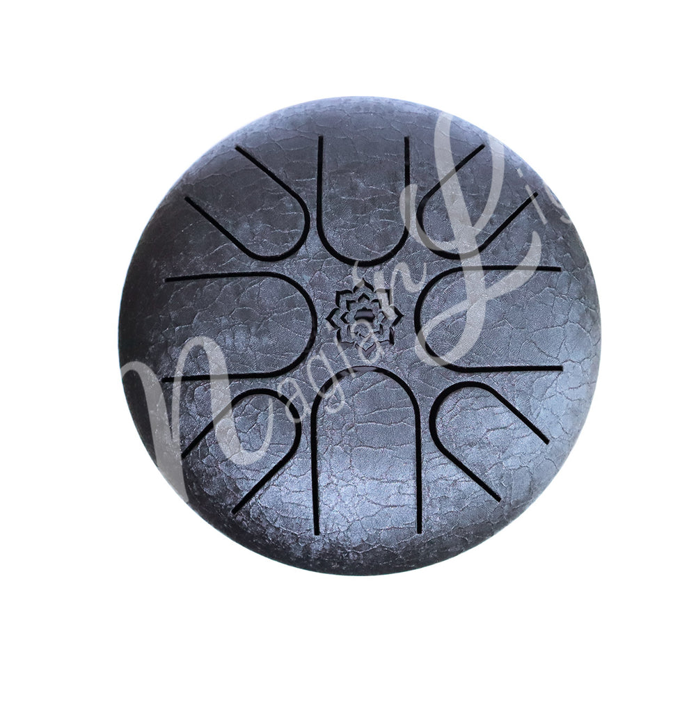 A top view of a blakc iron tongue drum with a speckled finish, featuring multiple U-shaped cutout tongues and a lotus flower symbol in the center.