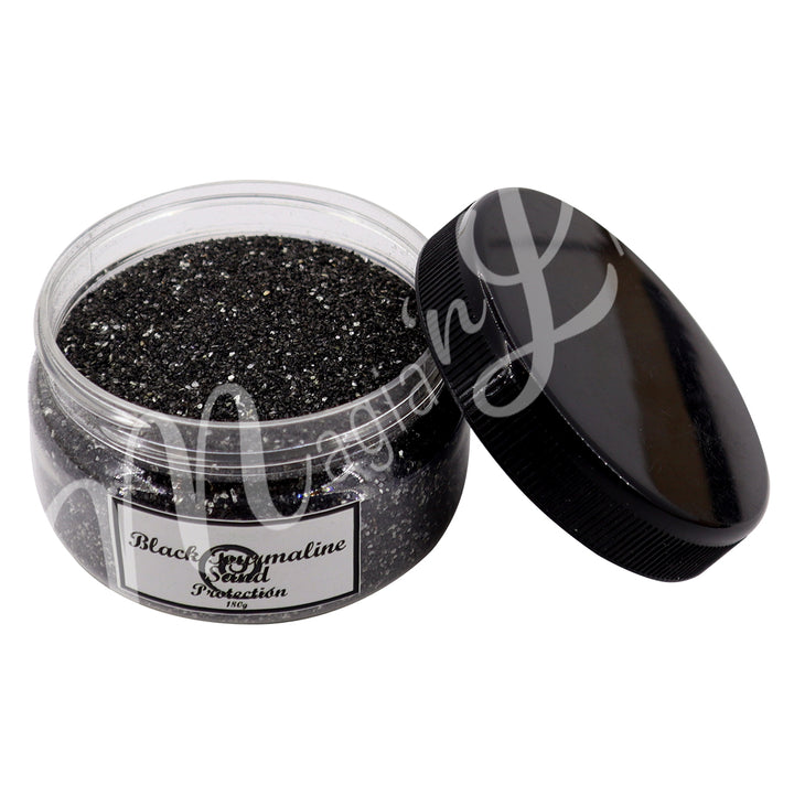 Clear plastic jar containing black stone sand with a black lid on the side. The label reads “Black Tourmaline Sand – Protection, 180 g.”