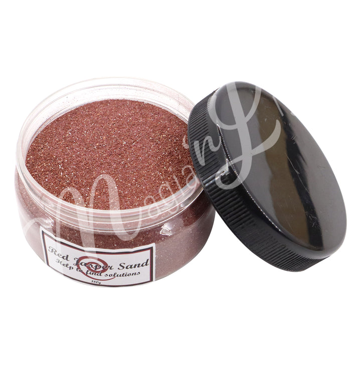 Clear plastic jar containing red stone sand with a black lid on the side. The label reads “Red Jasper Sand – Help to find solutions, 180 g.”