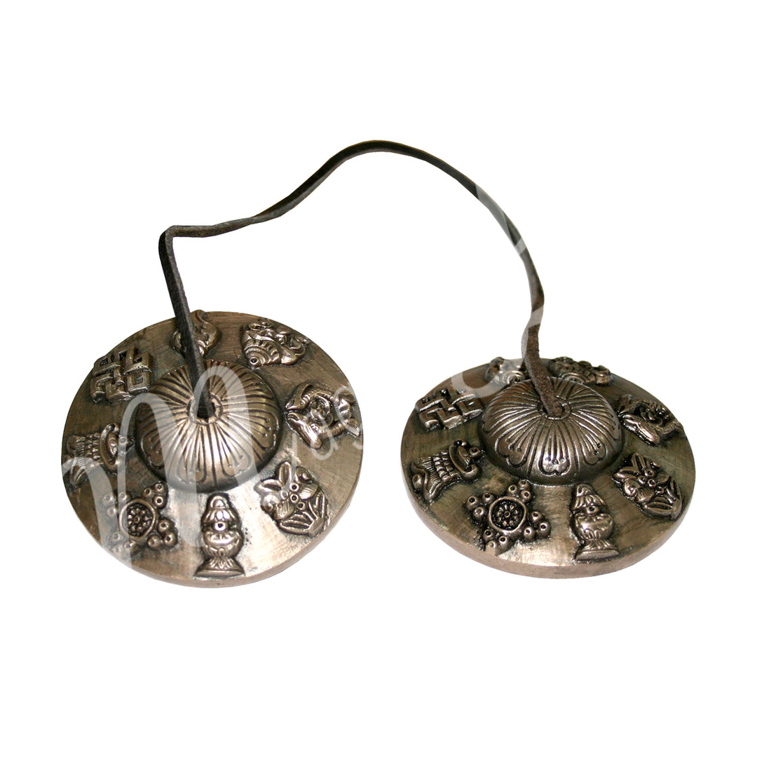 A pair of Tibetan tingsha cymbals connected by a leather cord, featuring engraved 8 auspicious symbols around the edges.