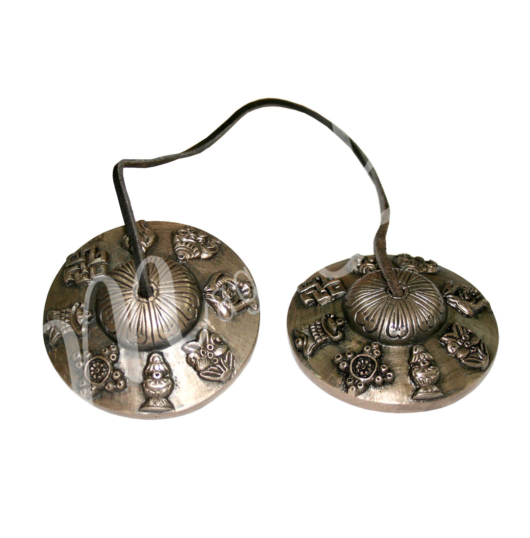 A pair of Tibetan tingsha cymbals connected by a leather cord, featuring engraved 8 auspicious symbols around the edges.