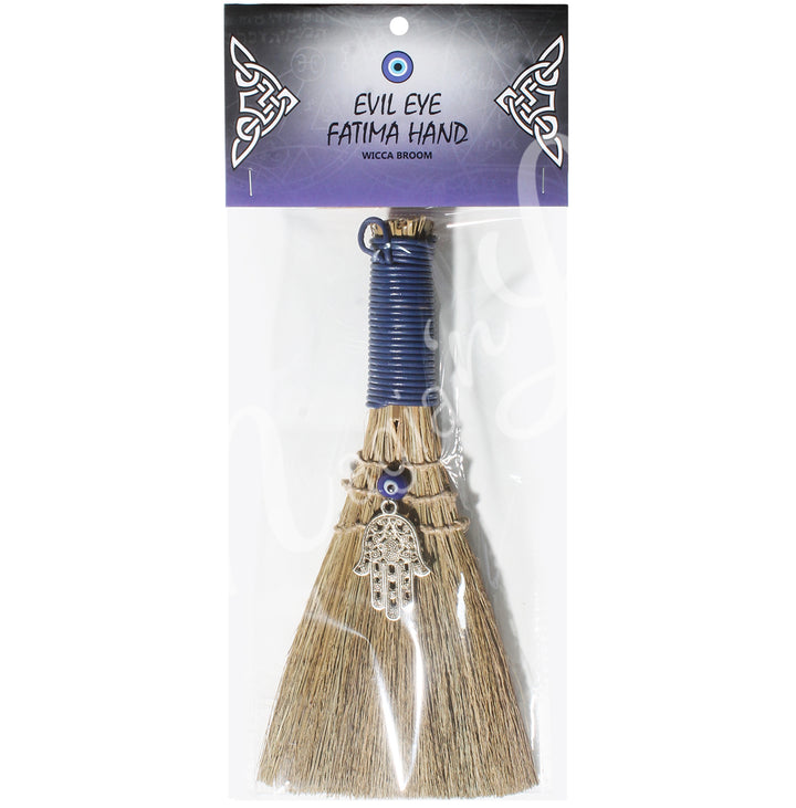 A witch's broom with a blue leather cord on top, featuring a straw base, an evil eye beads and Hand of Fatima. In a retail bag with the words: evil eye, fatima hand, wicca broom; on the card.