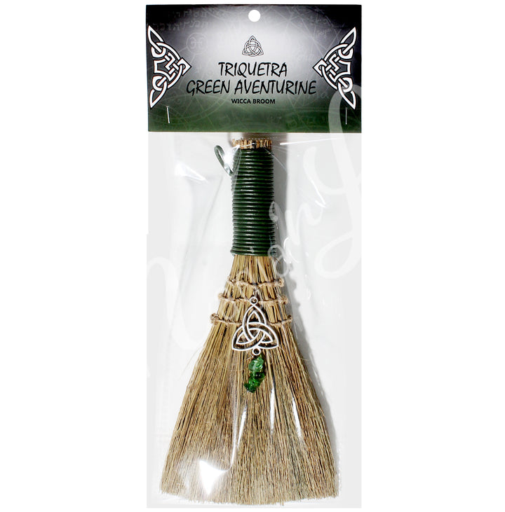 A witch's broom with a green leather cord on top, featuring a straw base decorated with a triquetra symbol and green Aventurine chips. In a retail bag with the words: Triquetra, green aventurine, wicca broom; on the card.