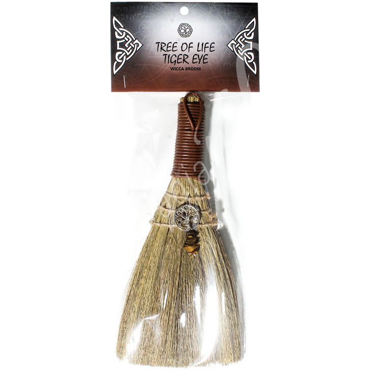 A witch's broom with a 'Tree of Life' charm and Tiger Eye stone, packaged in a clear plastic bag with a hanging card showing the product name.