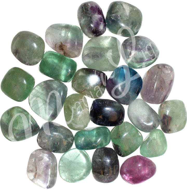 Collection of polished tumbled stones in shades of green, purple, blue, and black, arranged together in a circular pile.