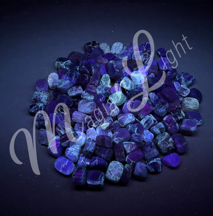 Collection of polished tumbled stones of fluorite, arranged together in a circular pile, seen under UV light.