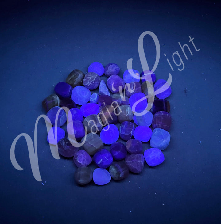 Collection of polished tumbled stones of rainbow fluorite, arranged together in a circular pile.
Seen under UV light.