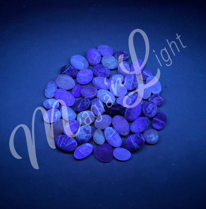 Collection of polished tumbled stones of pink and white fluorite, arranged together in a circular pile.
Seen under UV light.