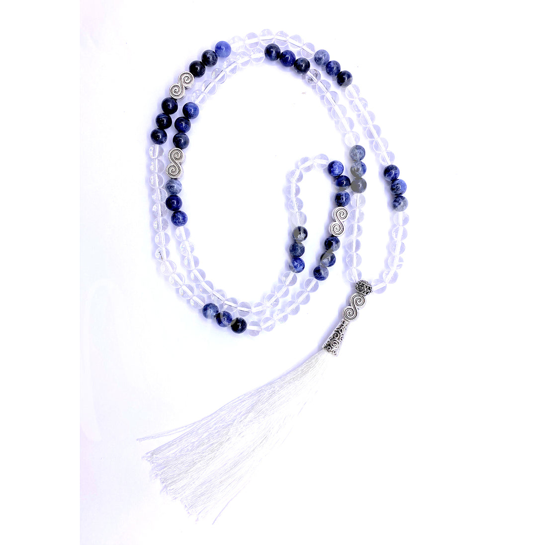 A crystal quartz and sodalite mala necklace with polished round beads with a double spiral charm and a long white tassel.