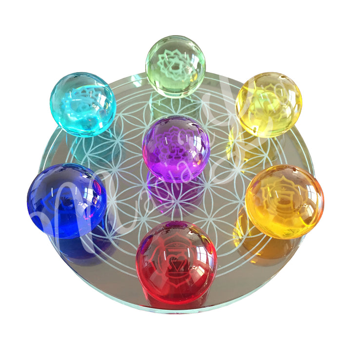 A set of seven chakra glass spheres, each with its respective symbol, displayed on a metallic coaster adorned with the Flower of Life design.