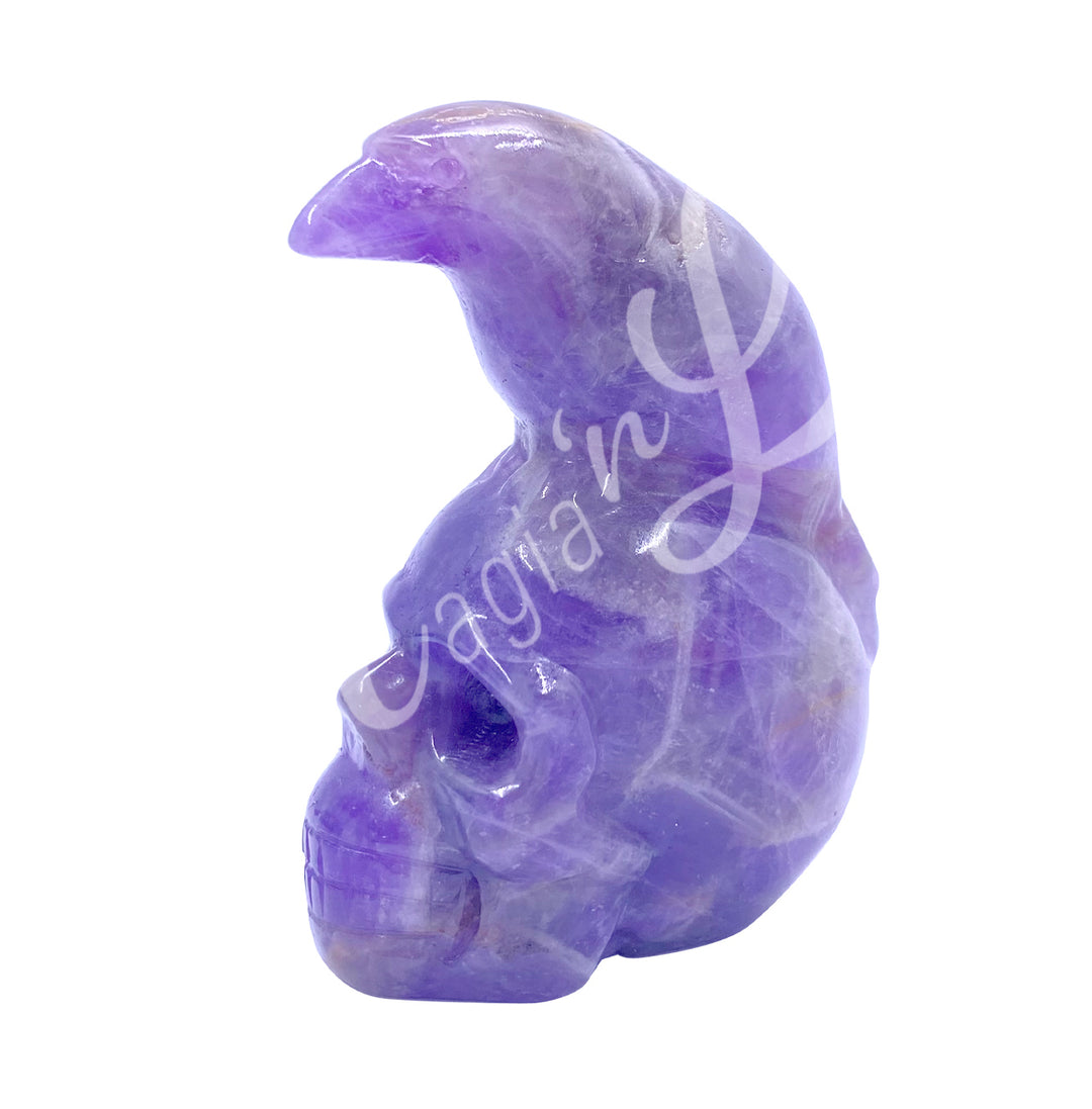 A polished raven on a skull carving made of amethyst.