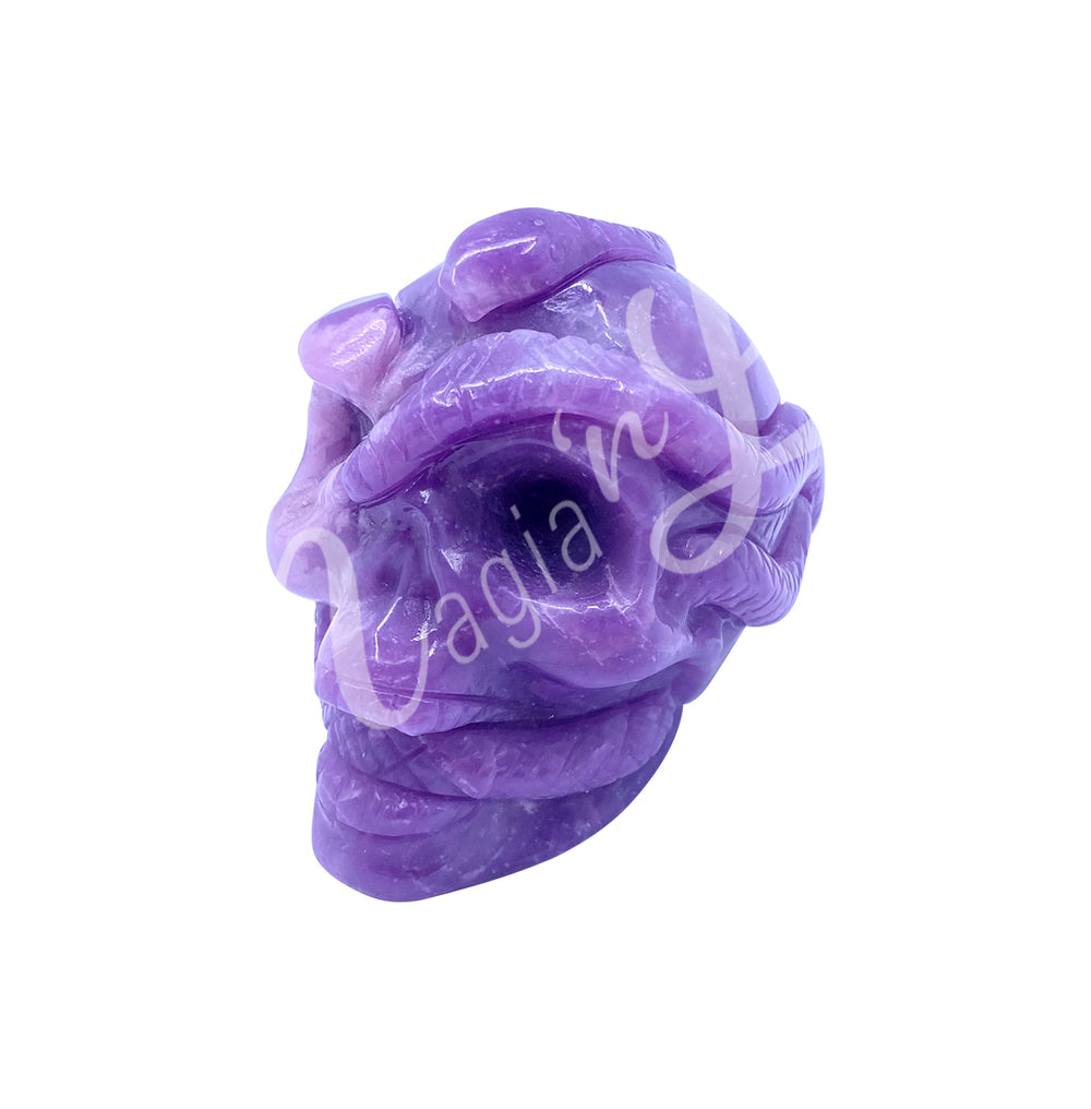 Polished gemstone skull with a snake carving made of lepidolite. Seen with an angle.