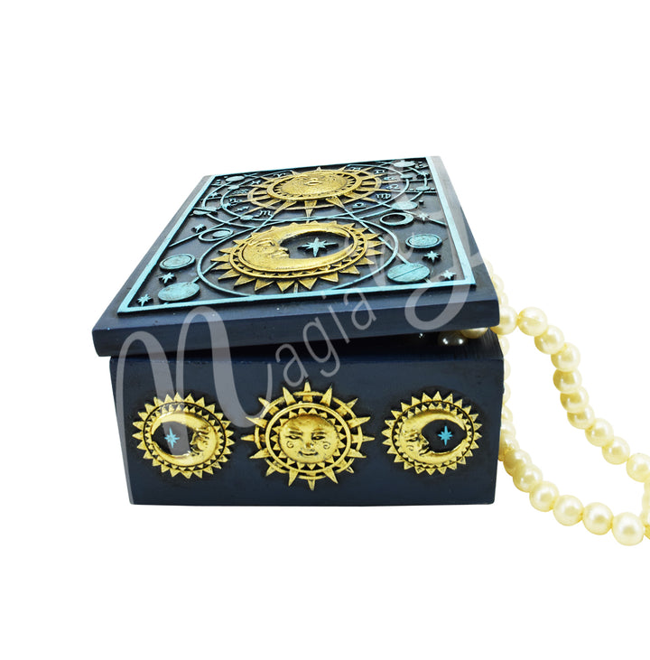 A navy blue box made of resin, adorned with celestial symbol with the lid slightly open to let a necklace pour out.