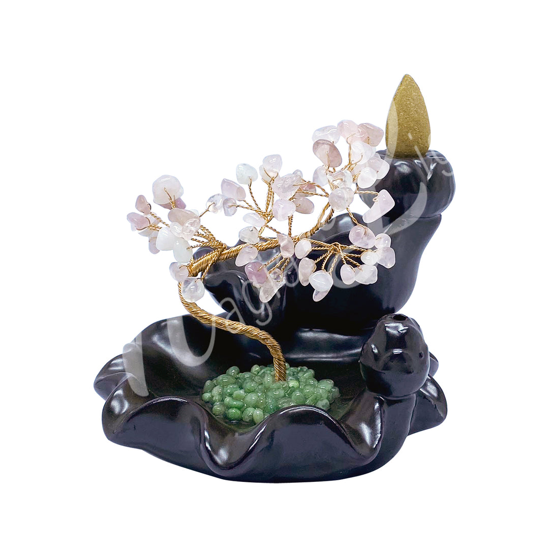 A gemstone bonsai tree with rose quartz crystal chips, mounted on an ornate black dish that also functions as a backflow cone burner.