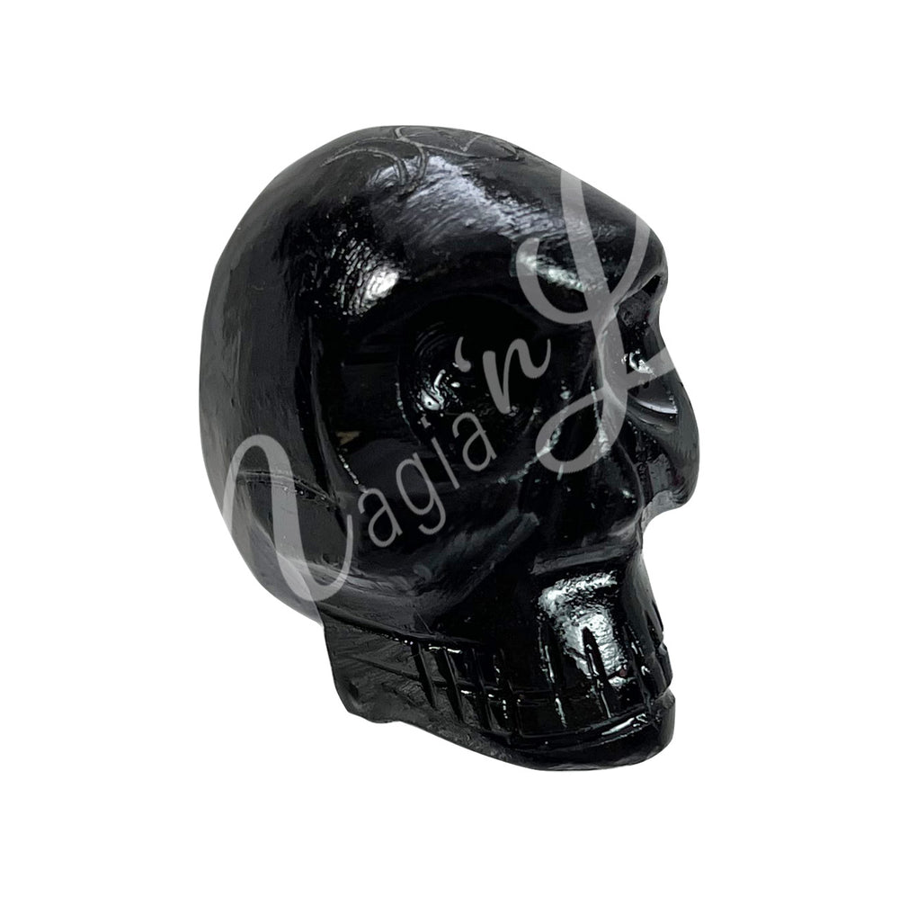 A polished skull carving made of smoky quartz, featuring an engraved triple moon with a pentacle at the center. Seen with an angle.