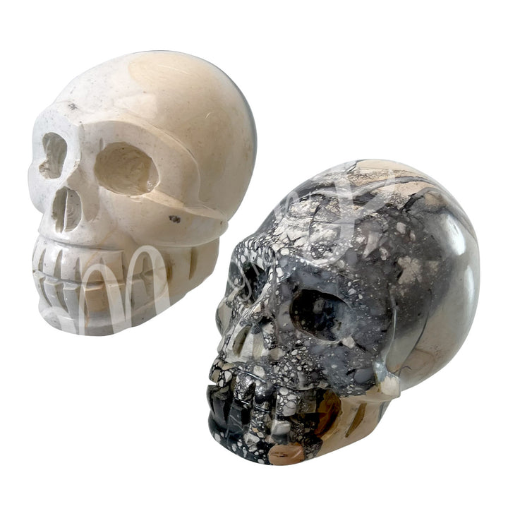 Two polished skull carvings made of Maligano jasper, shown in two different color shades.