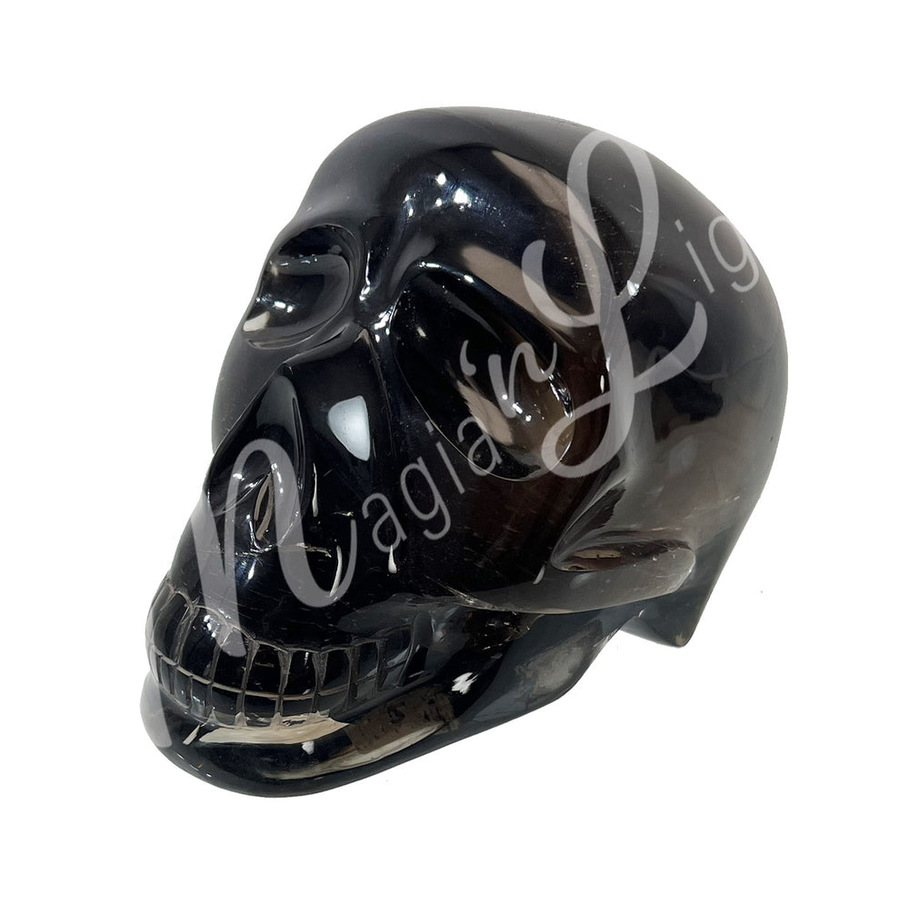 A polished skull carving with a visible crack, made of smoky quartz. Seen with an angle.