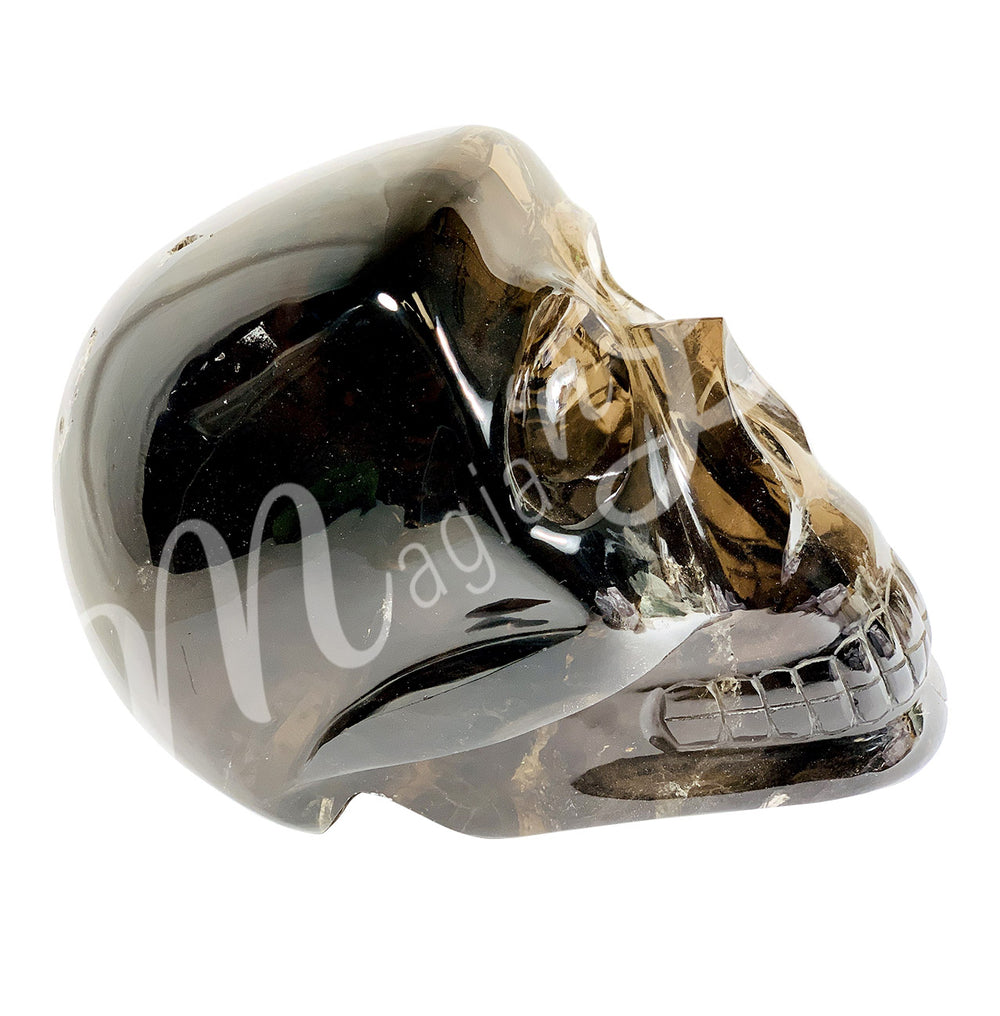 Polished gemstone skull carving made of smoky quartz. Seen from the side.