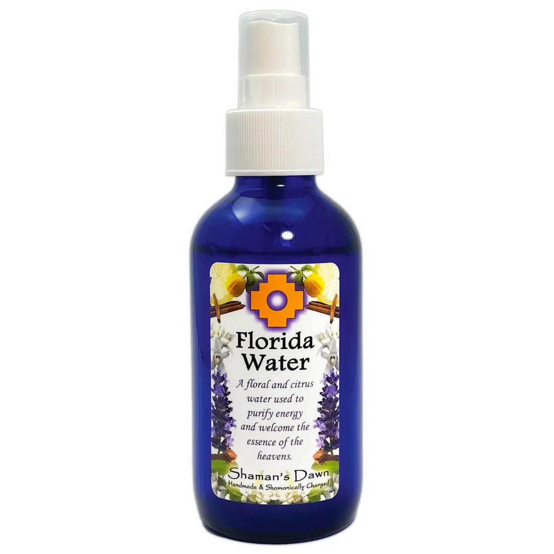 Blue spray bottle of Shaman’s Dawn Florida Water with a white pump top and a decorative label featuring flowers, citrus fruits, and cinnamon sticks. The label describes it as a floral and citrus water used to purify energy and welcome the essence of the heavens.