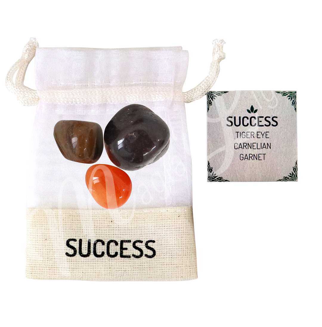 A white drawstring pouch labeled “SUCCESS,” displayed with three polished stones—Tiger Eye, Carnelian, and Garnet—alongside a tag that reads “SUCCESS: Tiger Eye, Carnelian, Garnet.”