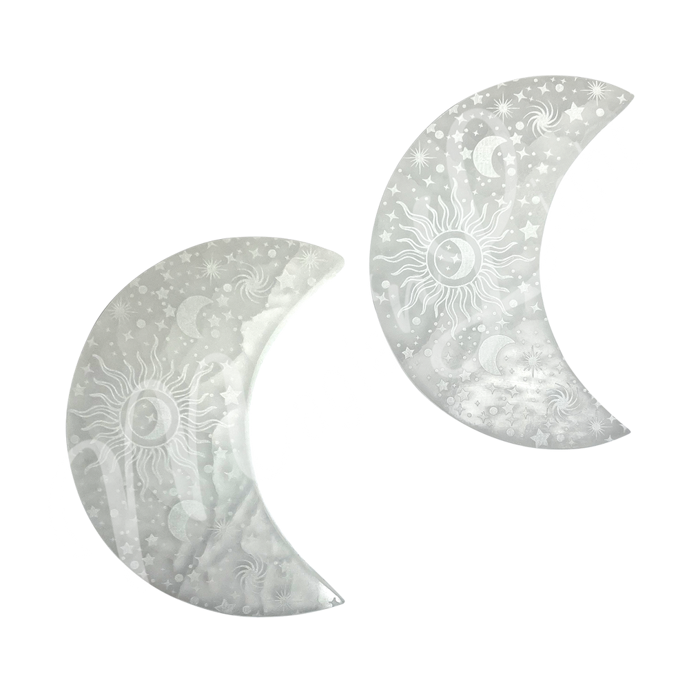 Two moon-shaped Selenite crystals engraved with stars, crescent moons, a central sun, and spiral galaxy designs.