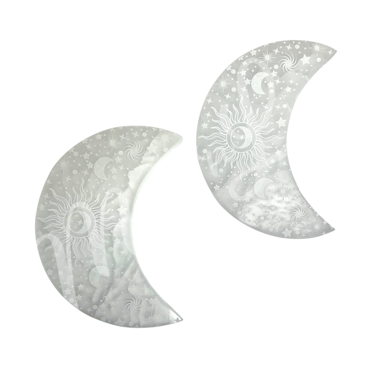 Two moon-shaped Selenite crystals engraved with stars, crescent moons, a central sun, and spiral galaxy designs.