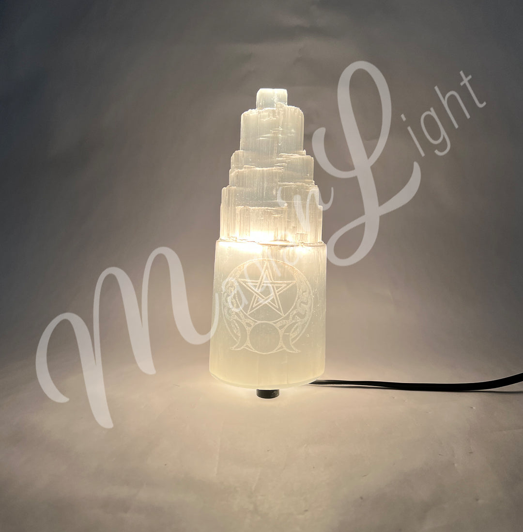 Selenite iceberg carving with black rubber feet. The lamp is engraved with a white triple moon and a pentacle, glowing in the dark.