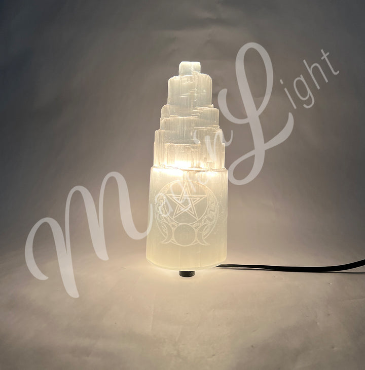 Selenite iceberg carving with black rubber feet. The lamp is engraved with a white triple moon and a pentacle, glowing in the dark.