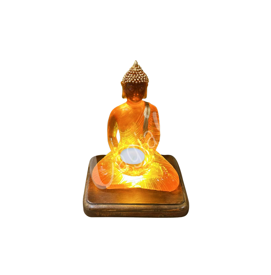 A resin lamp and statue representing the deity Buddha, holding a lotus flower in her hands, set on a rectangular wooden base. The lotus flower serves as a tealight holder. Shown with the light turned on.