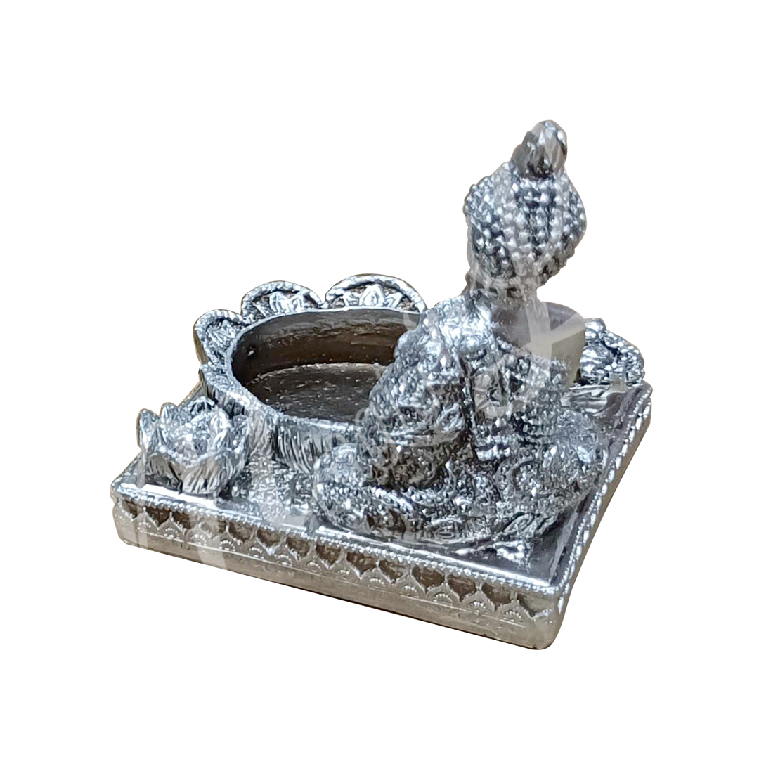 A silver-colored tealight and incense holder made of resin, featuring a Buddha with tealight and incense spaces at the front, shown from the back.