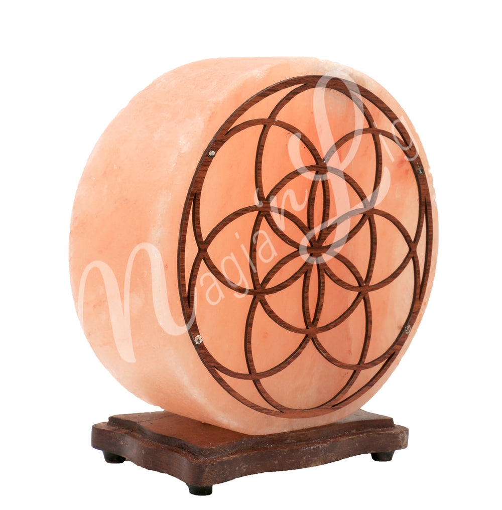 Angled view of a round Himalayan salt lamp mounted on a dark wooden base. The front is decorated with a seed of Life design wooden panel.