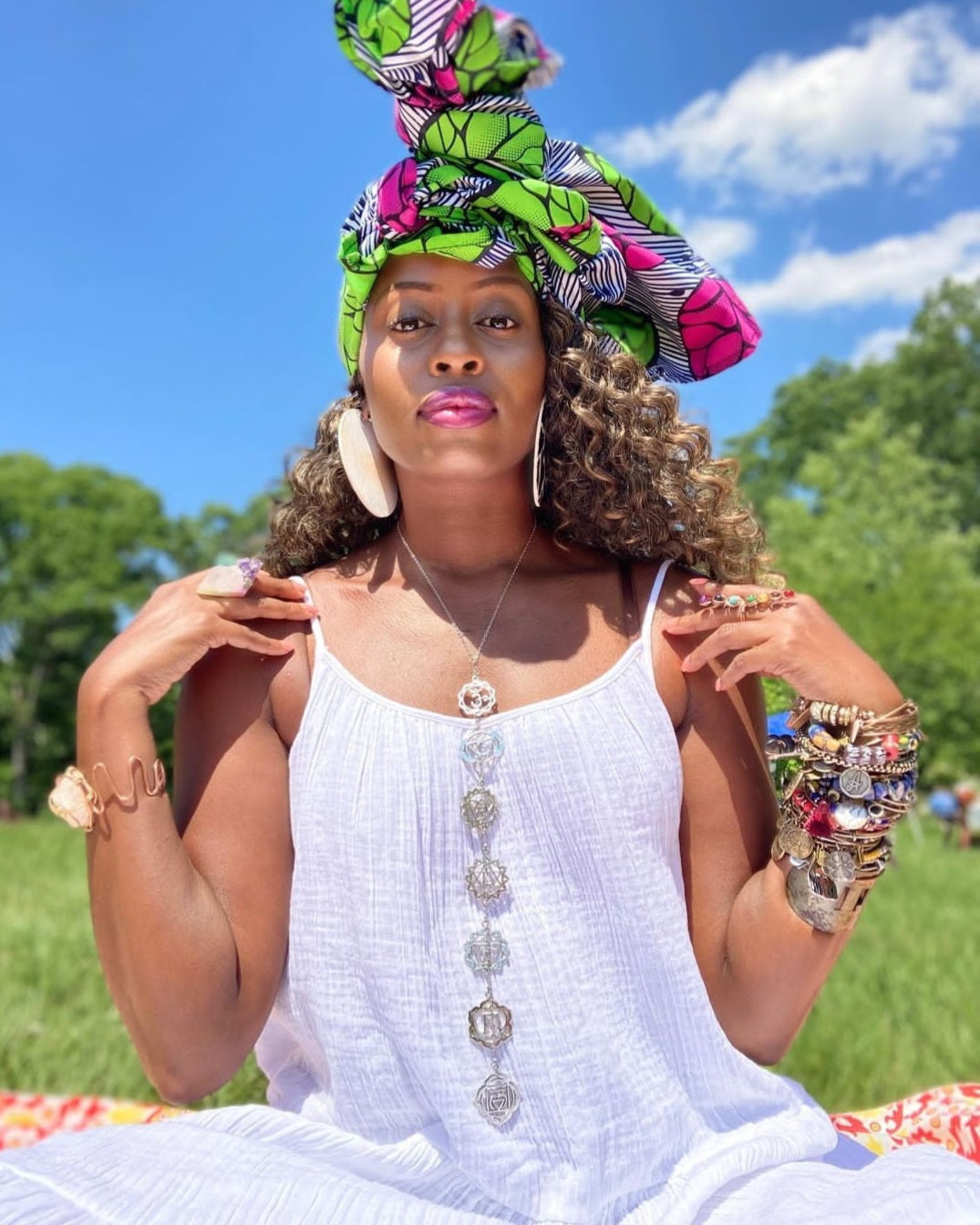 Woman in a white dress with colorful headwrap and jewelry outdoors